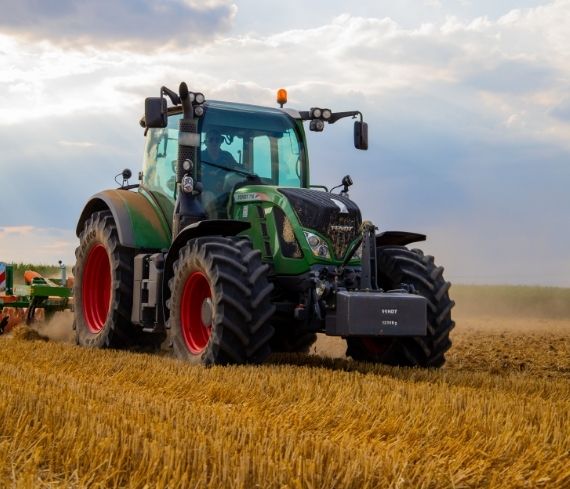 Trattore verde su campo di grano mietuto.