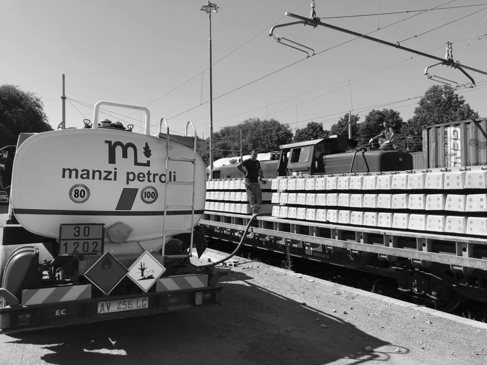 Camion cisterna rifornisce treno merci su binario ferroviario.